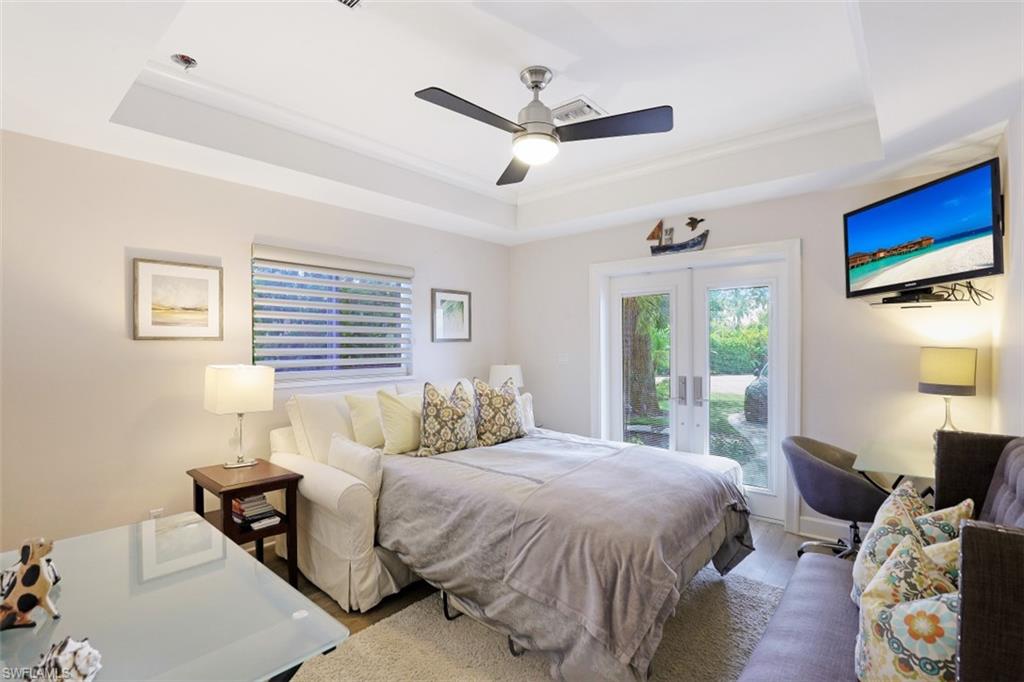 Bedroom with a tray ceiling, access to outside, french doors, wood finished floors, and ceiling fan