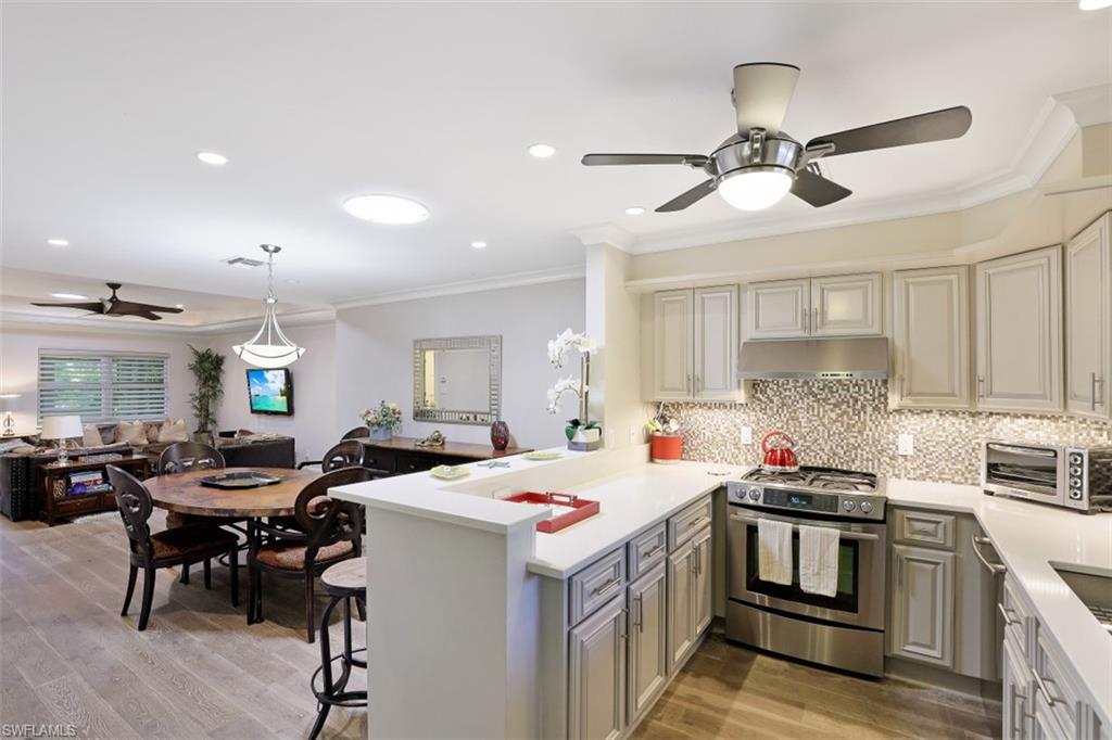 Kitchen featuring stainless steel gas range oven, ceiling fan, under cabinet range hood, open floor plan, and ornamental molding