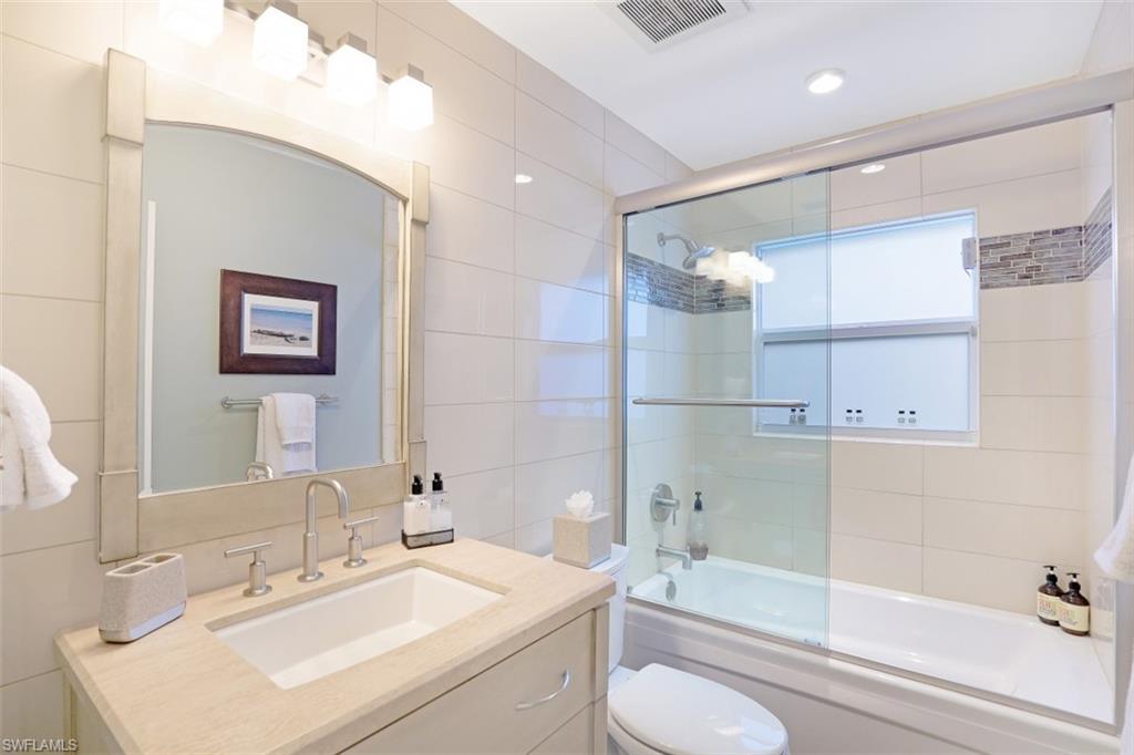 Full bathroom featuring tile walls, shower / bath combination with glass door, toilet, and vanity