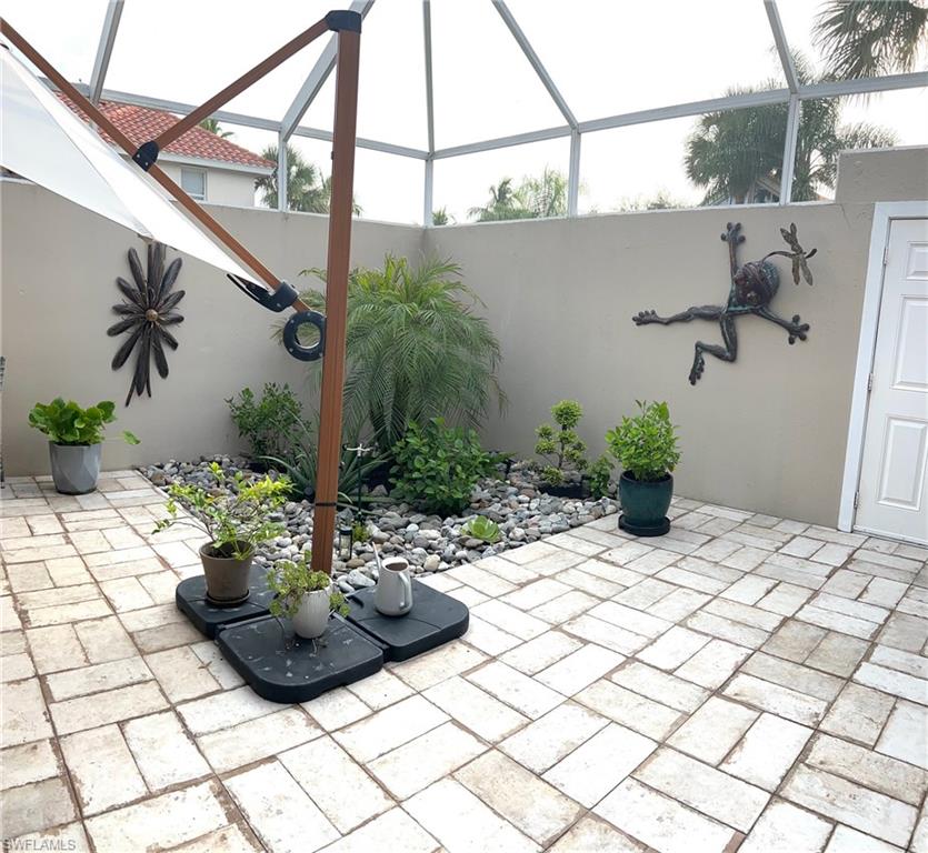 Screened-in courtyard featuring light-toned paver flooring, a rock garden with mature plantings, and solid perimeter walls