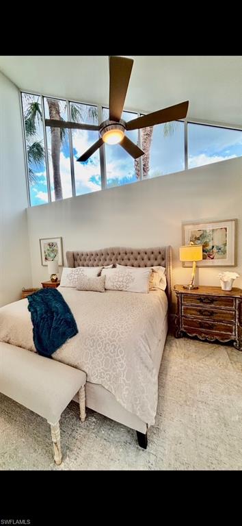 Vaulted ceiling bedroom featuring transom windows, a ceiling fan with integrated lighting, a tufted headboard, and light-toned flooring