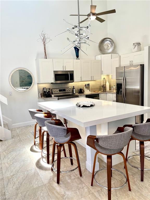 Kitchen featuring a large central island with a solid surface countertop, white cabinetry, stainless steel appliances, and a tiled backsplash