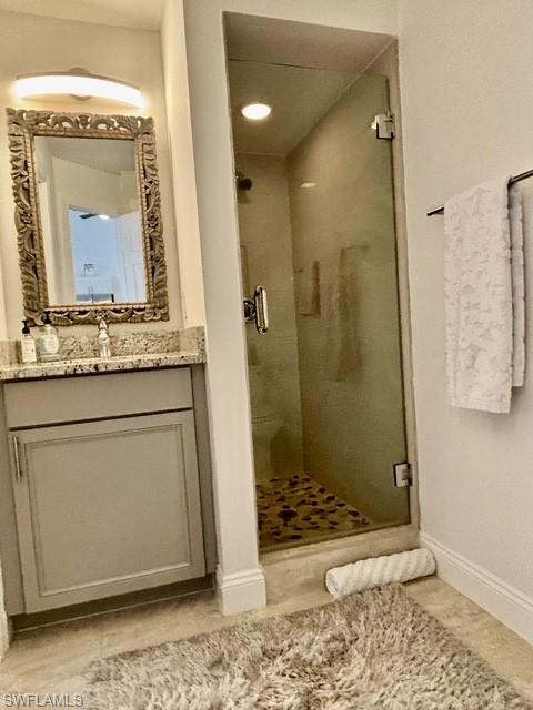 Full glass shower enclosure featuring a mosaic tile floor, alongside a vanity with a stone countertop, an ornate framed mirror, and a wall-mounted light fixture