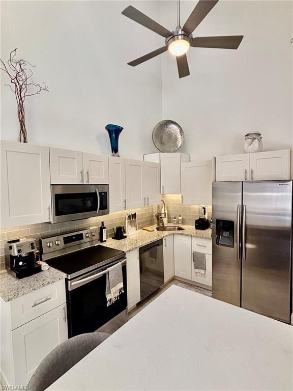 Modern kitchen featuring vaulted ceilings, stainless steel appliances, light cabinetry, granite-style countertops, and a tiled backsplash