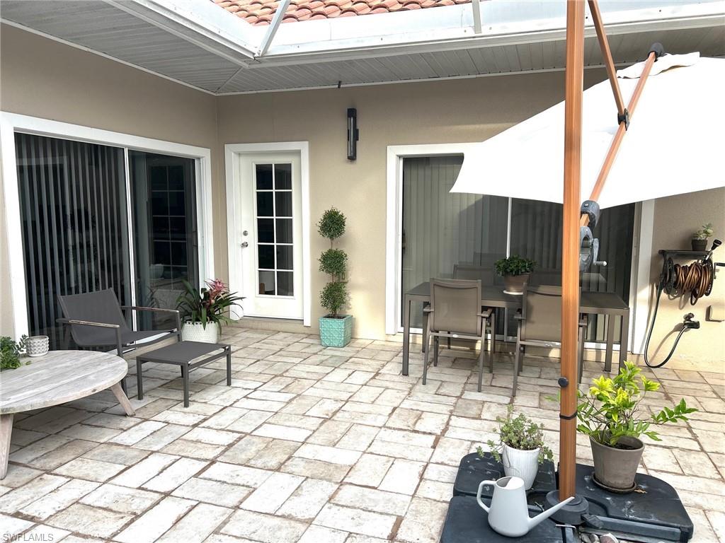 Expansive paver patio with a covered outdoor area, multiple sliding glass doors, a French-style entry door, and exterior sconce lighting