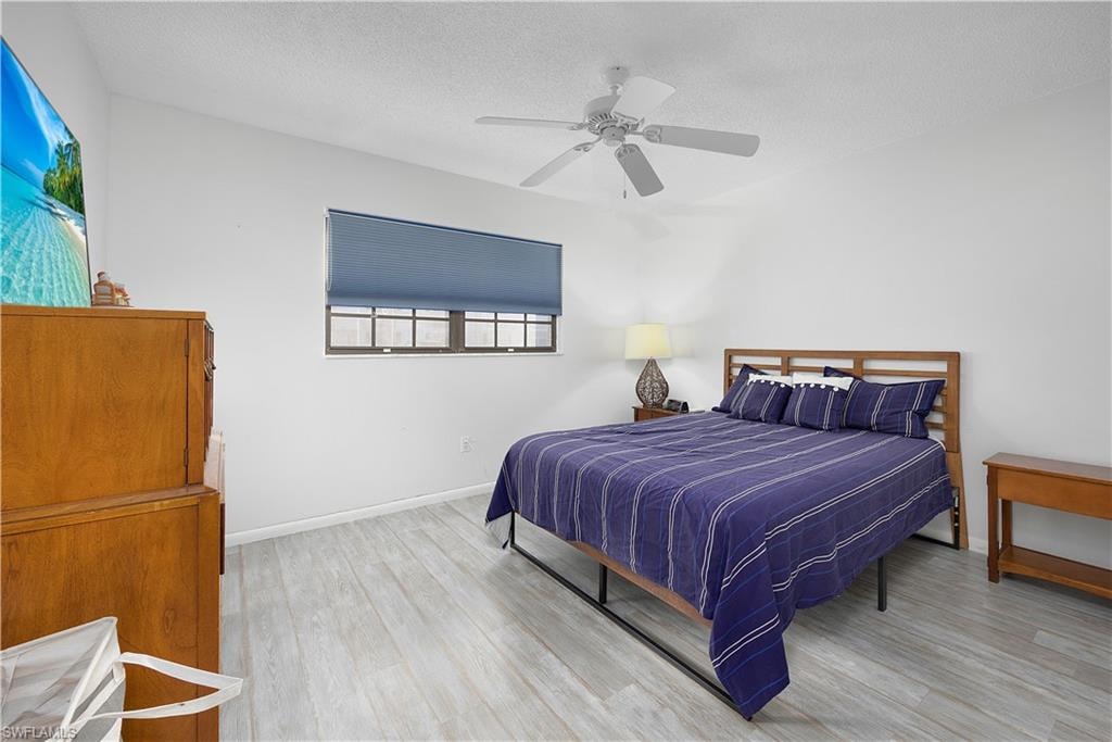 Bedroom with light wood-type flooring, ceiling fan, and a textured ceiling