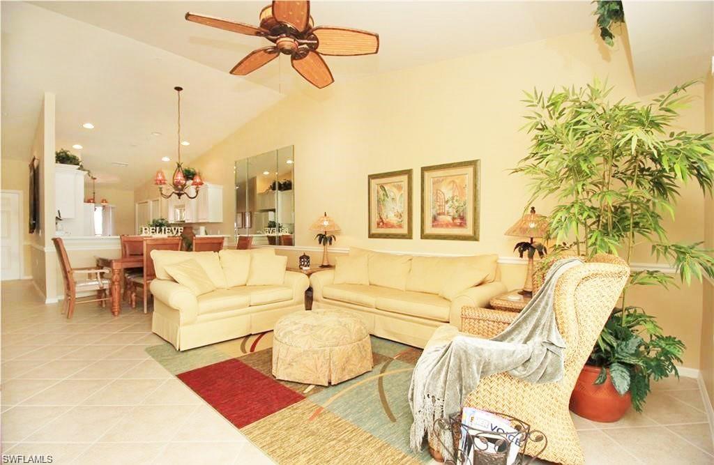 Living room with ceiling fan, light tile patterned flooring, and lofted ceiling
