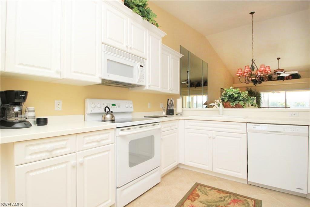 Kitchen featuring white appliances, white cabinetry, vaulted ceiling, and a notable chandelier