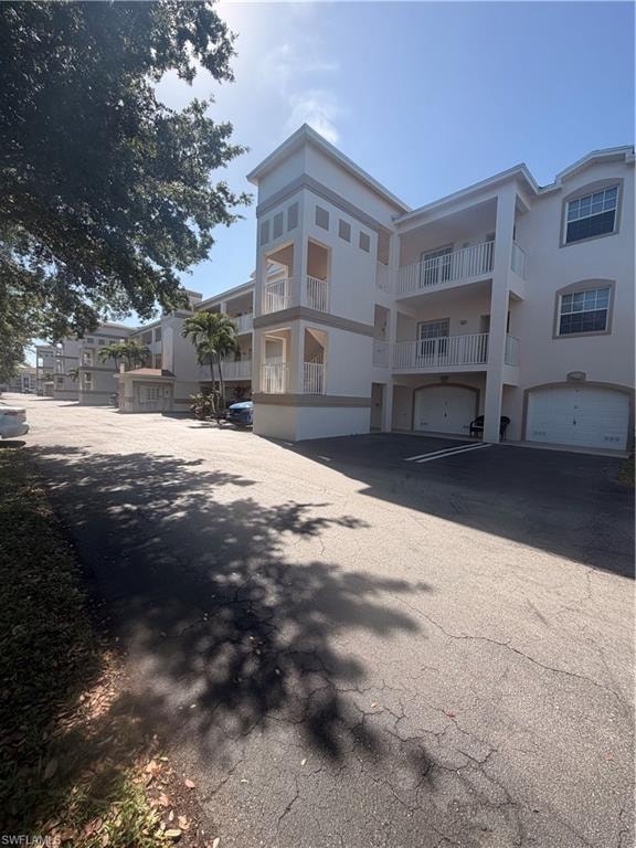 Multi-story building featuring stucco exterior with contrasting trim bands, multiple private balconies with white railings, arched garage doors, and visible palm trees