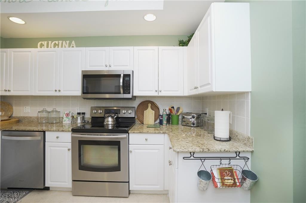 Kitchen featuring appliances with stainless steel finishes, light stone countertops, tasteful backsplash, and white cabinets