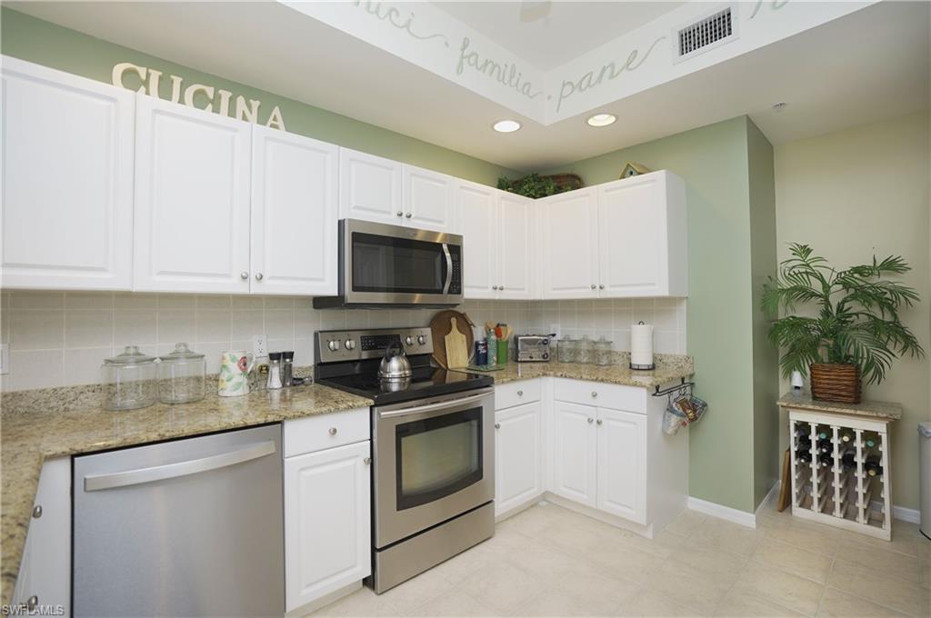 Kitchen featuring light stone counters, white cabinets, appliances with stainless steel finishes, and tasteful backsplash
