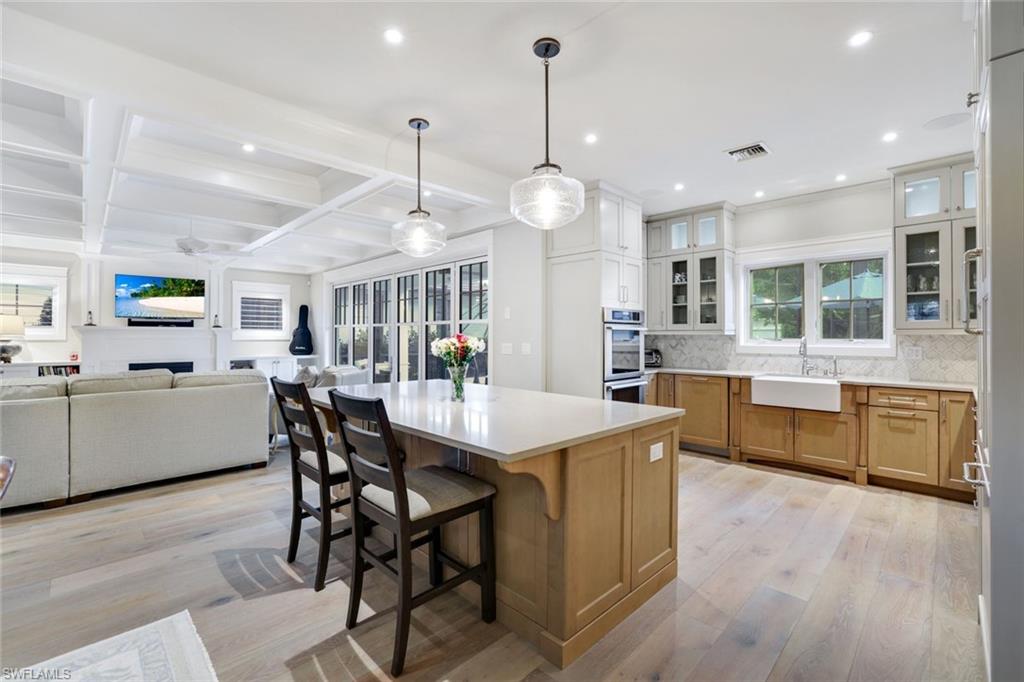 Kitchen with decorative backsplash, sink, a spacious island, light hardwood / wood-style flooring, and decorative light fixtures