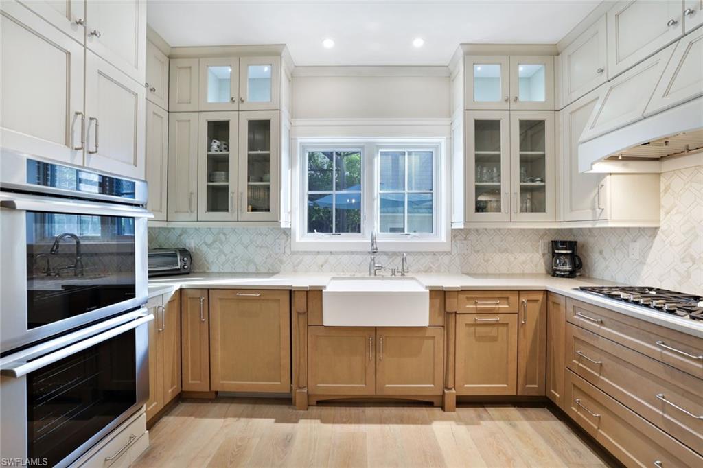 Kitchen with sink, appliances with stainless steel finishes, custom range hood, backsplash, and light hardwood / wood-style flooring