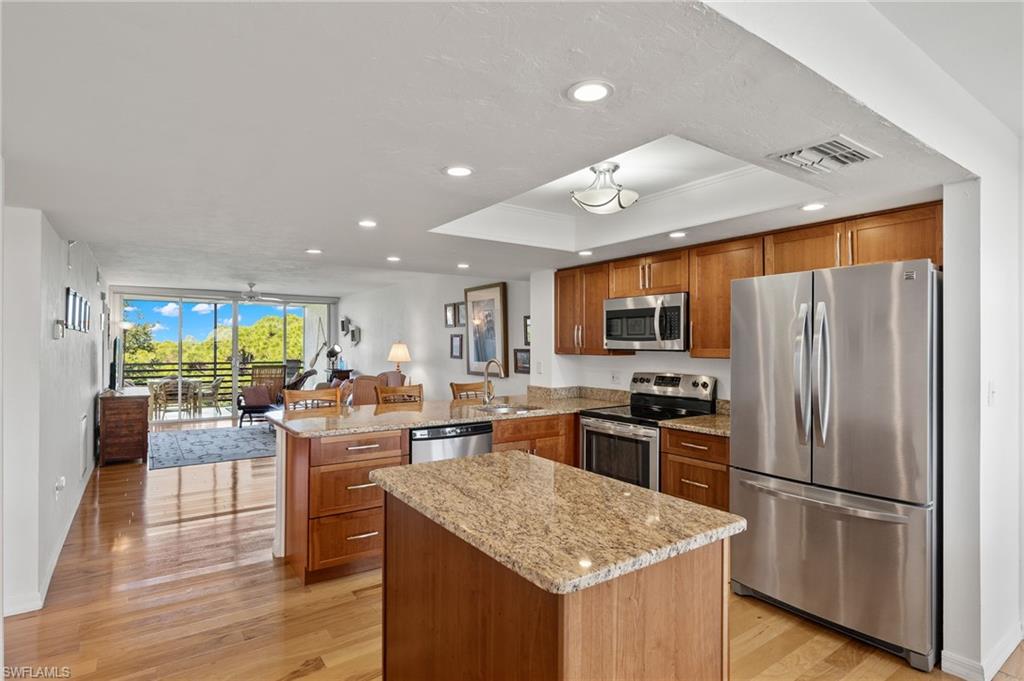 Open-concept kitchen featuring wood-finish cabinetry, granite countertops, and stainless steel appliances