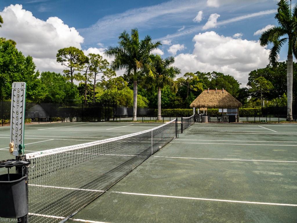 Regulation tennis court featuring a net, scorekeeper, and thatched-roof shelter