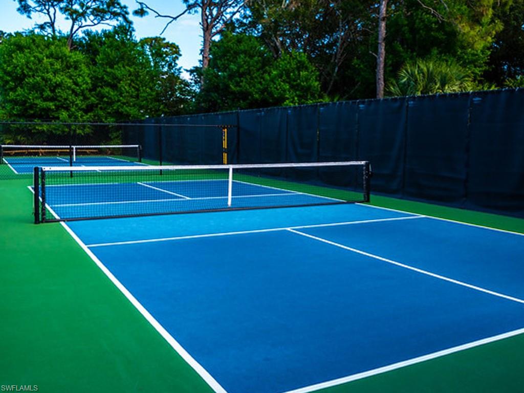 Dual pickleball courts featuring blue and green surfacing with white line markings, black netting, and a privacy screen perimeter