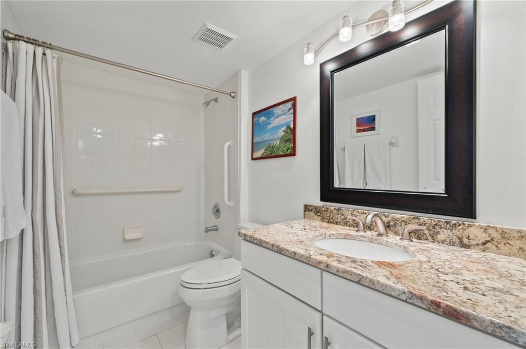 Bathroom featuring a white vanity with a light-colored stone countertop, an undermount sink, and a framed mirror