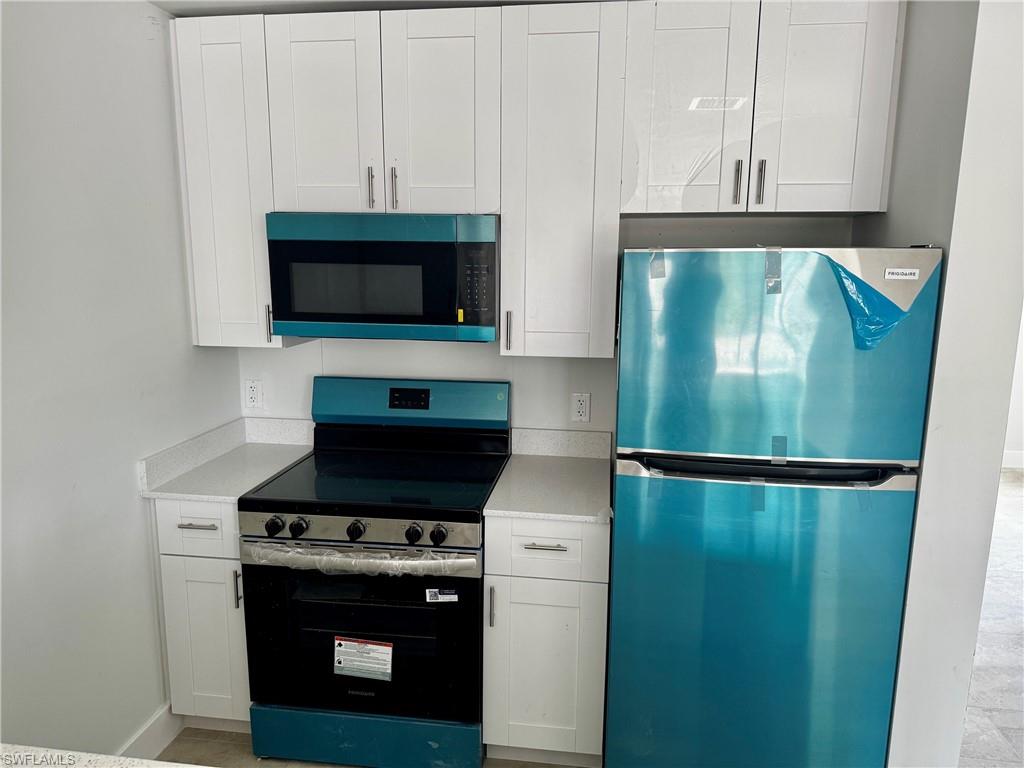 Modern kitchen featuring white shaker cabinetry with brushed nickel hardware, light-toned countertops, and new stainless steel appliances including a refrigerator, electric range, and microwave