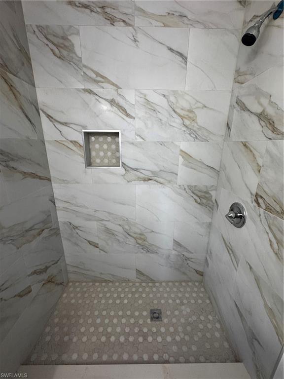 Shower featuring large-format wall tiles with a natural stone pattern and a hexagonal mosaic tile floor