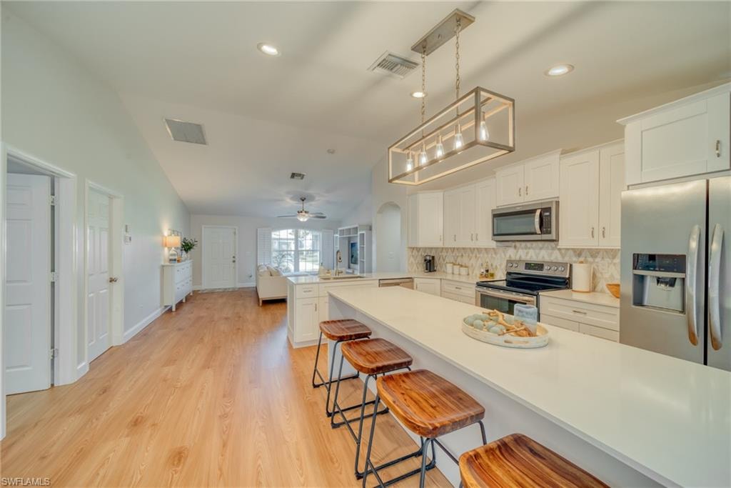 Kitchen with a breakfast bar, stainless steel appliances, white cabinetry, a peninsula, and light wood finished floors