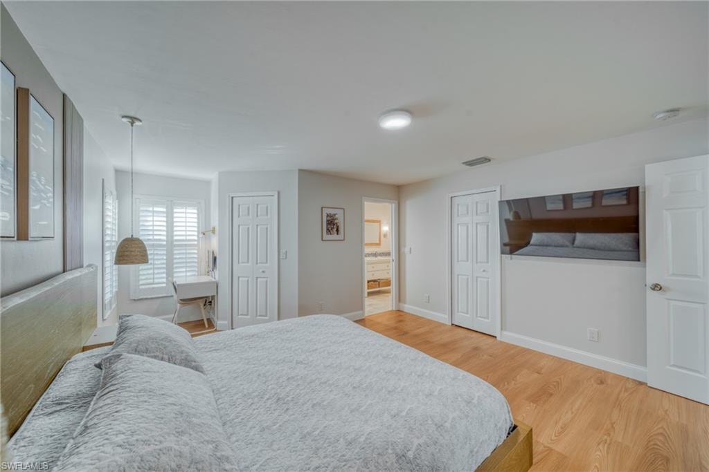 Bedroom with light wood-type flooring, two closets, and ensuite bath