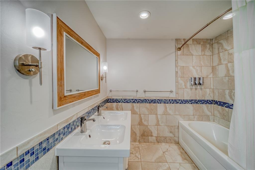 Full bathroom featuring tile walls, double vanity, wainscoting, shower / bath combination with curtain, and recessed lighting