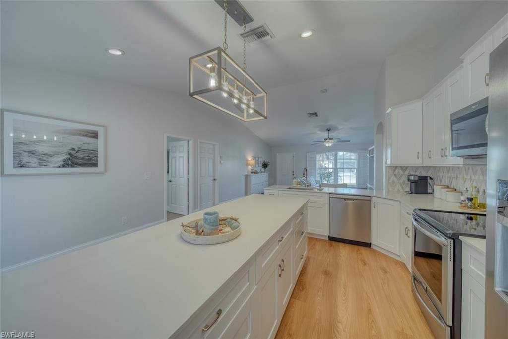 Kitchen with stainless steel appliances, white cabinets, a peninsula, light wood finished floors, and vaulted ceiling