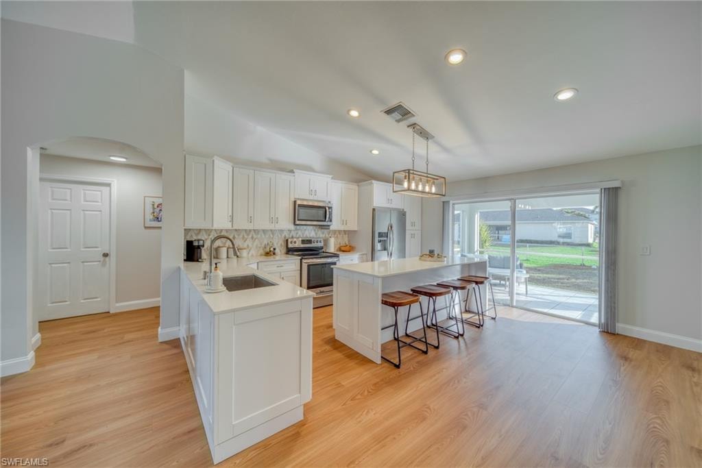 Kitchen featuring a kitchen bar, stainless steel appliances, white cabinets, arched walkways, and a kitchen island