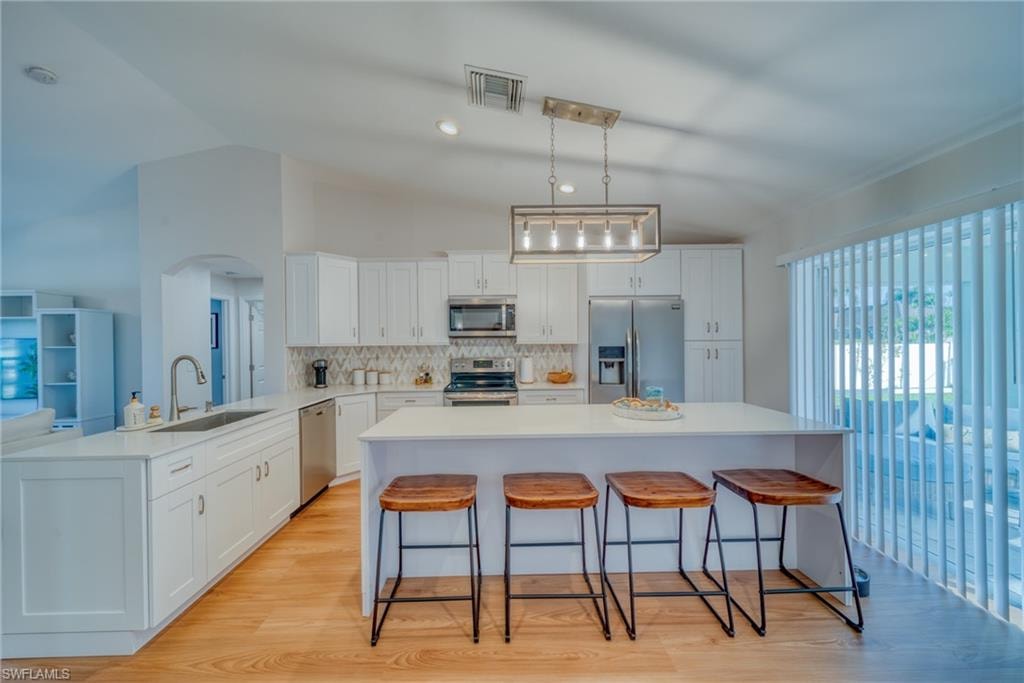 Kitchen with a kitchen bar, stainless steel appliances, white cabinets, light wood-type flooring, and backsplash