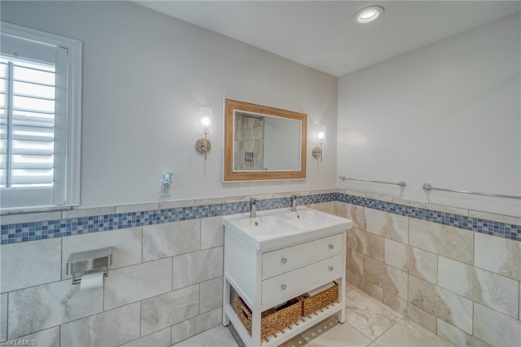 Full bath featuring double vanity, tile walls, wainscoting, light tile patterned floors, and recessed lighting