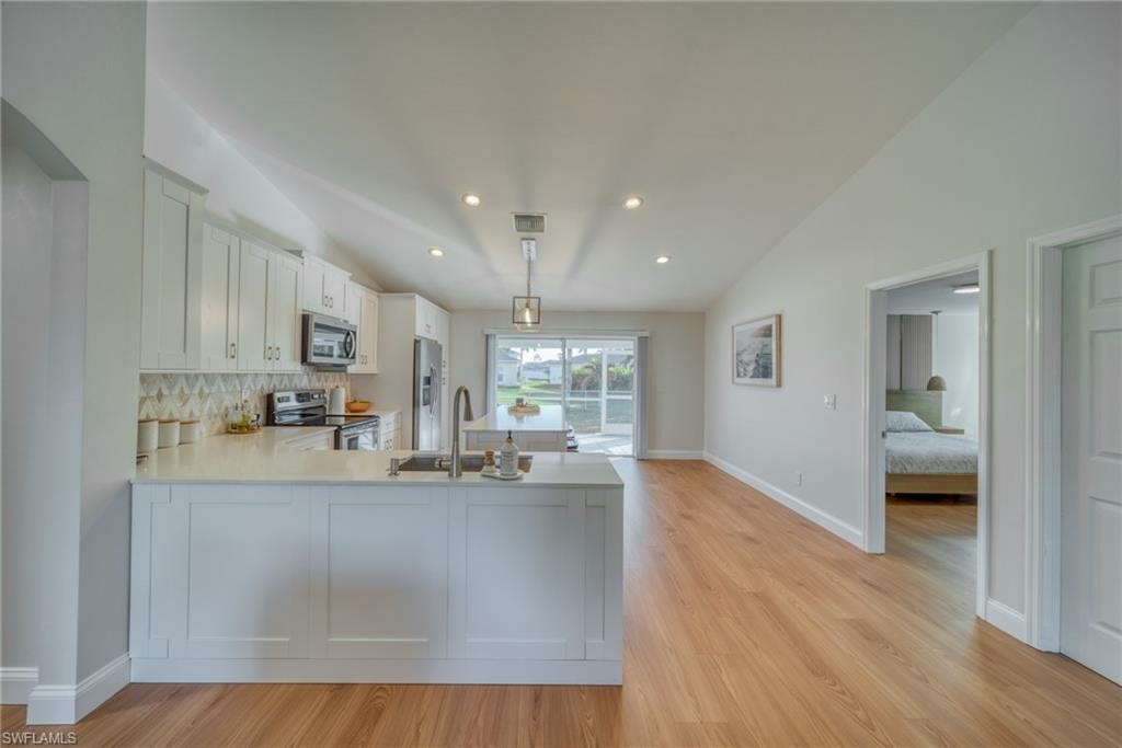 Kitchen featuring vaulted ceiling, white cabinetry, stainless steel appliances, light wood-type flooring, and a peninsula