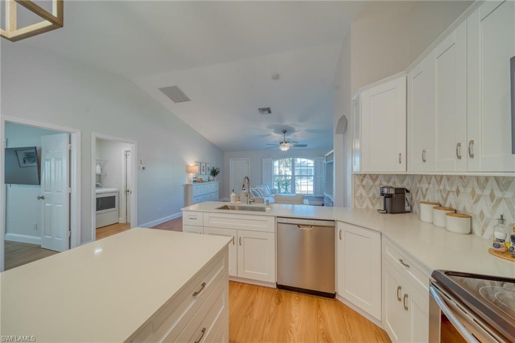 Kitchen featuring a peninsula, stainless steel appliances, white cabinets, light wood-style flooring, and vaulted ceiling