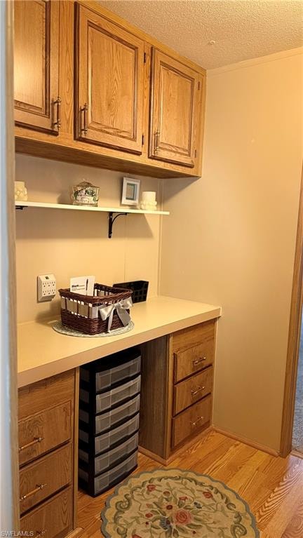 Built-in desk area can be used for a variety of purposes and features wood cabinetry, a light-colored countertop, overhead storage, and wood-like flooring.