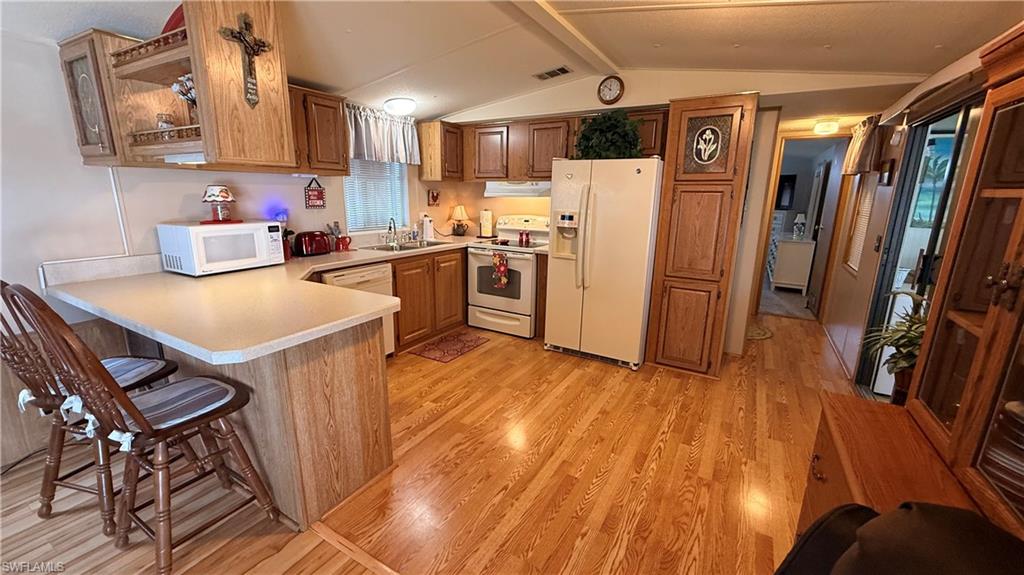Kitchen featuring wood-look flooring, a built-in breakfast bar, white appliances, and a double basin sink with disposal & dishwasher.