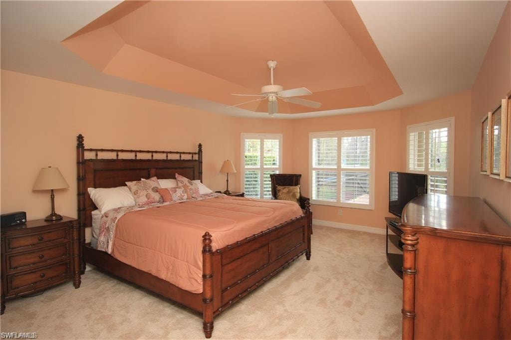 Bedroom with ceiling fan, a raised ceiling, and light carpet