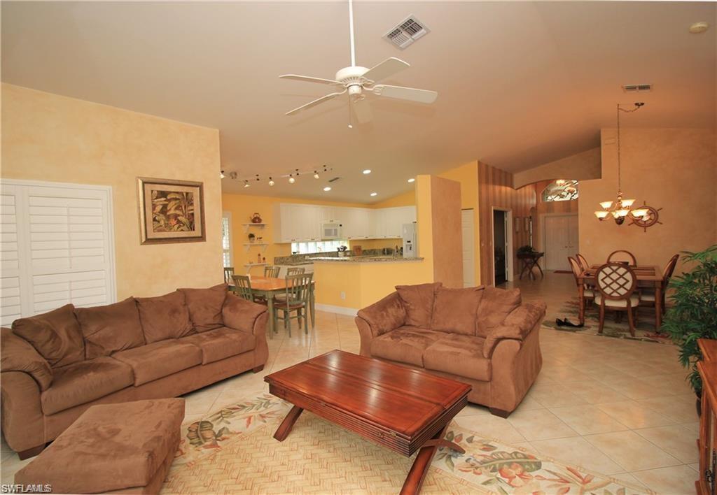 Tiled living room featuring vaulted ceiling and ceiling fan with notable chandelier
