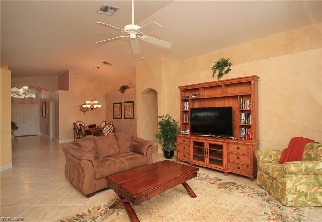 Living room featuring lofted ceiling, light tile patterned floors, and ceiling fan with notable chandelier