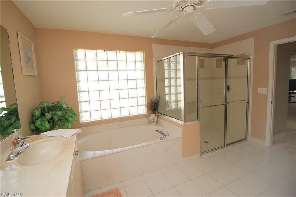 Bathroom with tile patterned flooring, vanity, ceiling fan, and plus walk in shower
