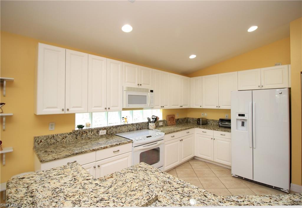 Kitchen featuring white appliances, white cabinets, and lofted ceiling