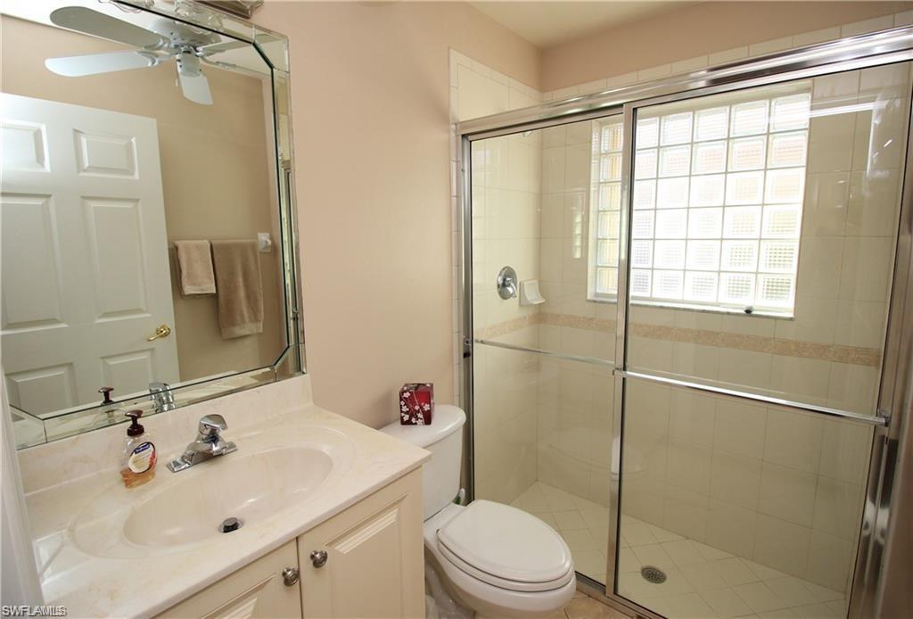 Bathroom with walk in shower, toilet, ceiling fan, and vanity