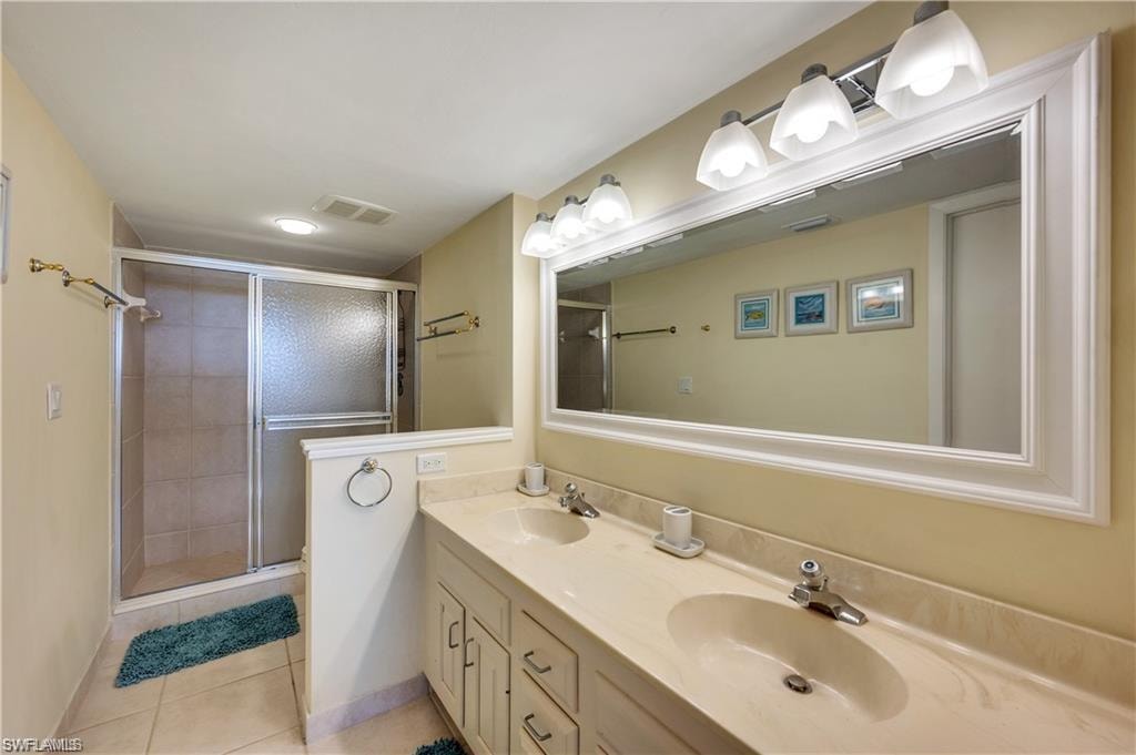 Bathroom featuring a shower with shower door, double sink vanity, and tile patterned flooring