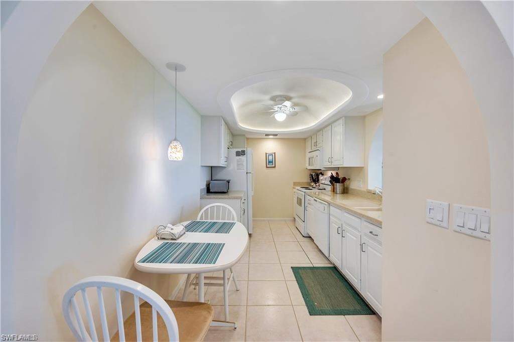 Kitchen with white appliances, decorative light fixtures, light tile patterned floors, white cabinetry, and ceiling fan