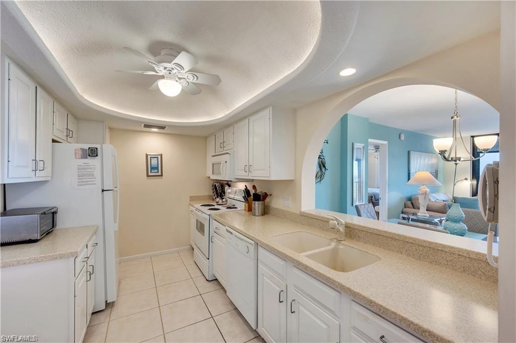 Kitchen with white appliances, white cabinets, sink, ceiling fan with notable chandelier, and light tile patterned flooring