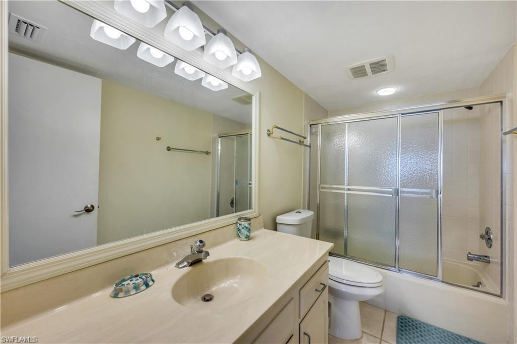 Full bathroom featuring tile patterned flooring, toilet, shower / bath combination with glass door, and vanity