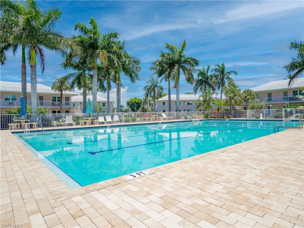 Community swimming pool featuring a paver surround, white safety fence, and surrounding tropical landscaping