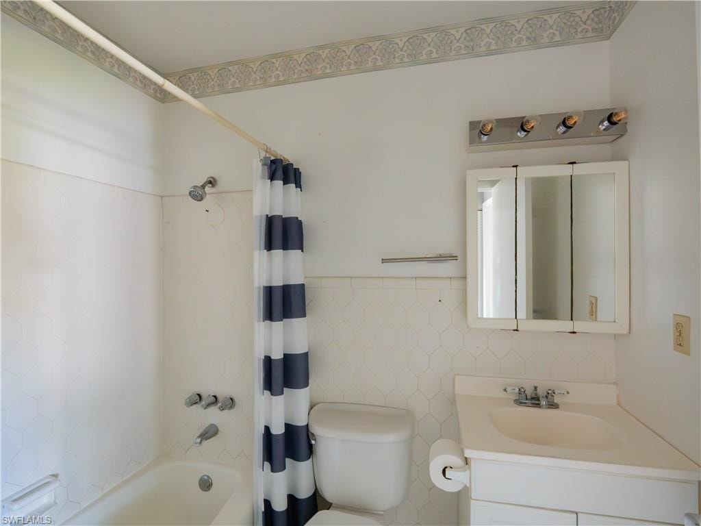 Bathroom featuring a built-in bathtub with shower, white tile surround, and a vanity with an integrated sink