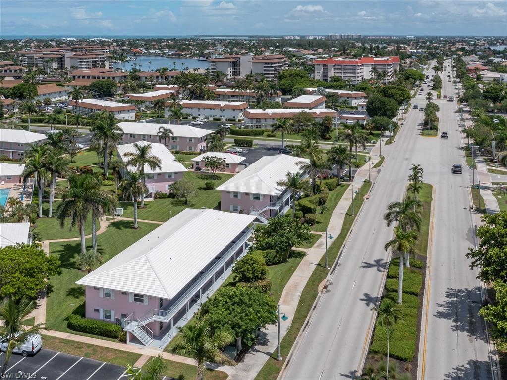 Aerial perspective showcasing multiple two-story residential buildings with light pink facades and white roofs, surrounded by mature palm trees and lush green landscaping