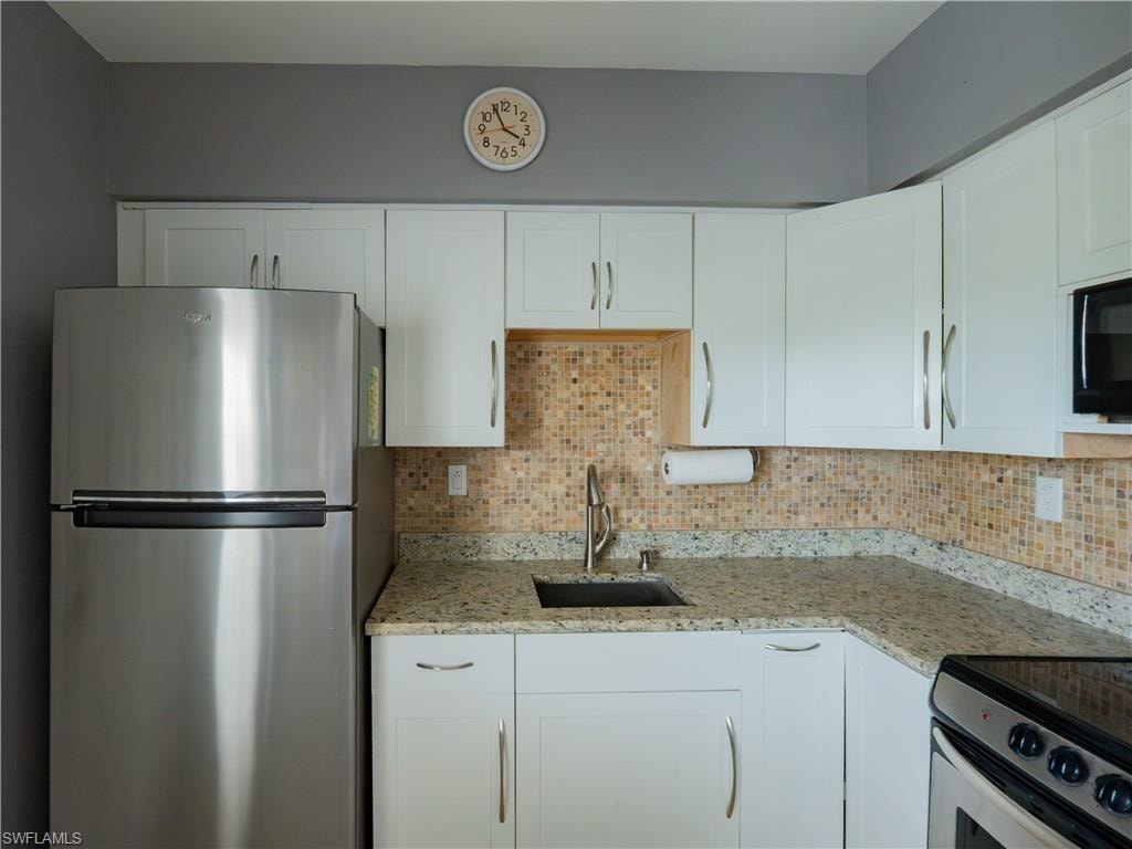 Kitchen featuring white cabinetry with brushed nickel hardware, light granite countertops, and a full tile backsplash
