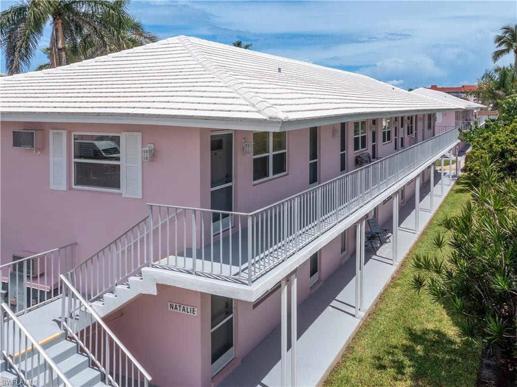 Two-story residential building featuring a tile roof, light pink exterior, and white window shutters