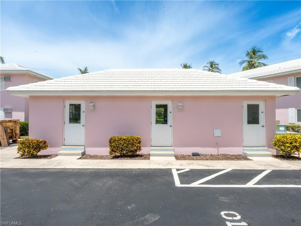 Pink exterior building featuring a white tile roof, multiple entry doors with glass inserts, and exterior wall sconces